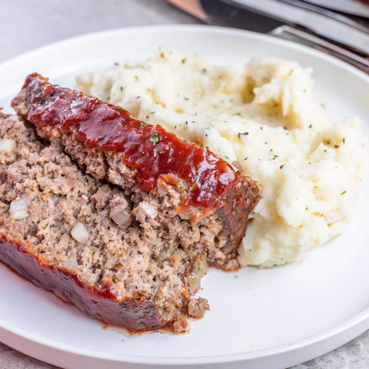 Classic meatloaf topped with savory glaze, served alongside creamy mashed potatoes.  