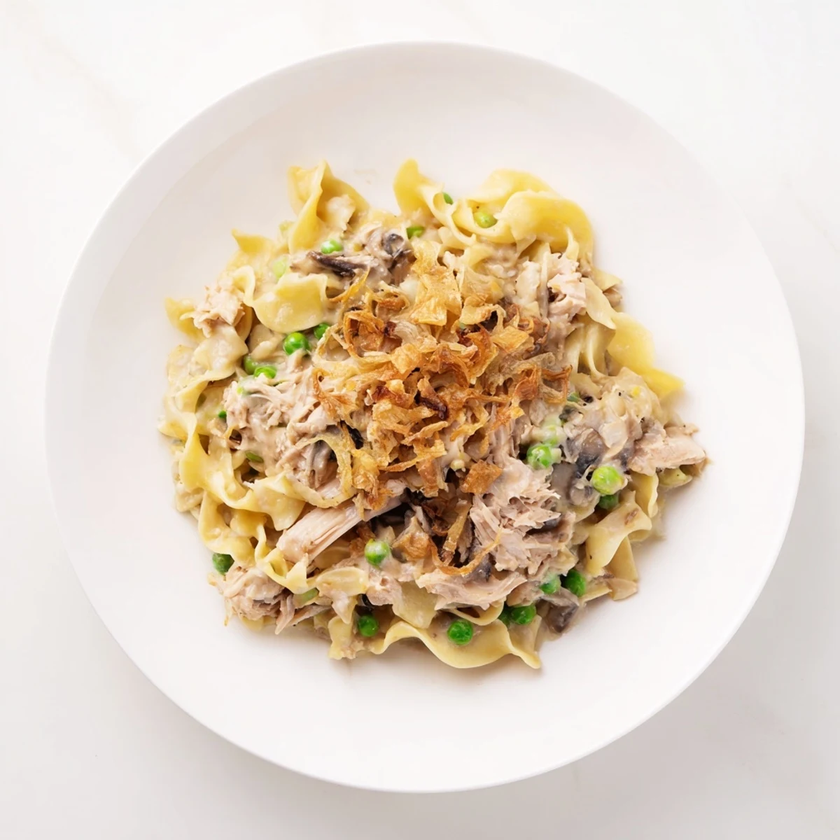 A close-up view of creamy tuna noodle casserole topped with crispy onions, bubbling inside a baking dish.