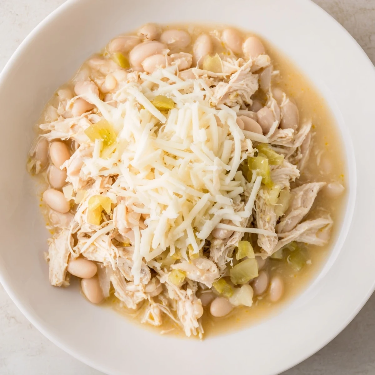 Steaming bowl of 35-Minute White Cheddar Apple Chicken Chili, topped with extra shredded cheese and fresh apple.