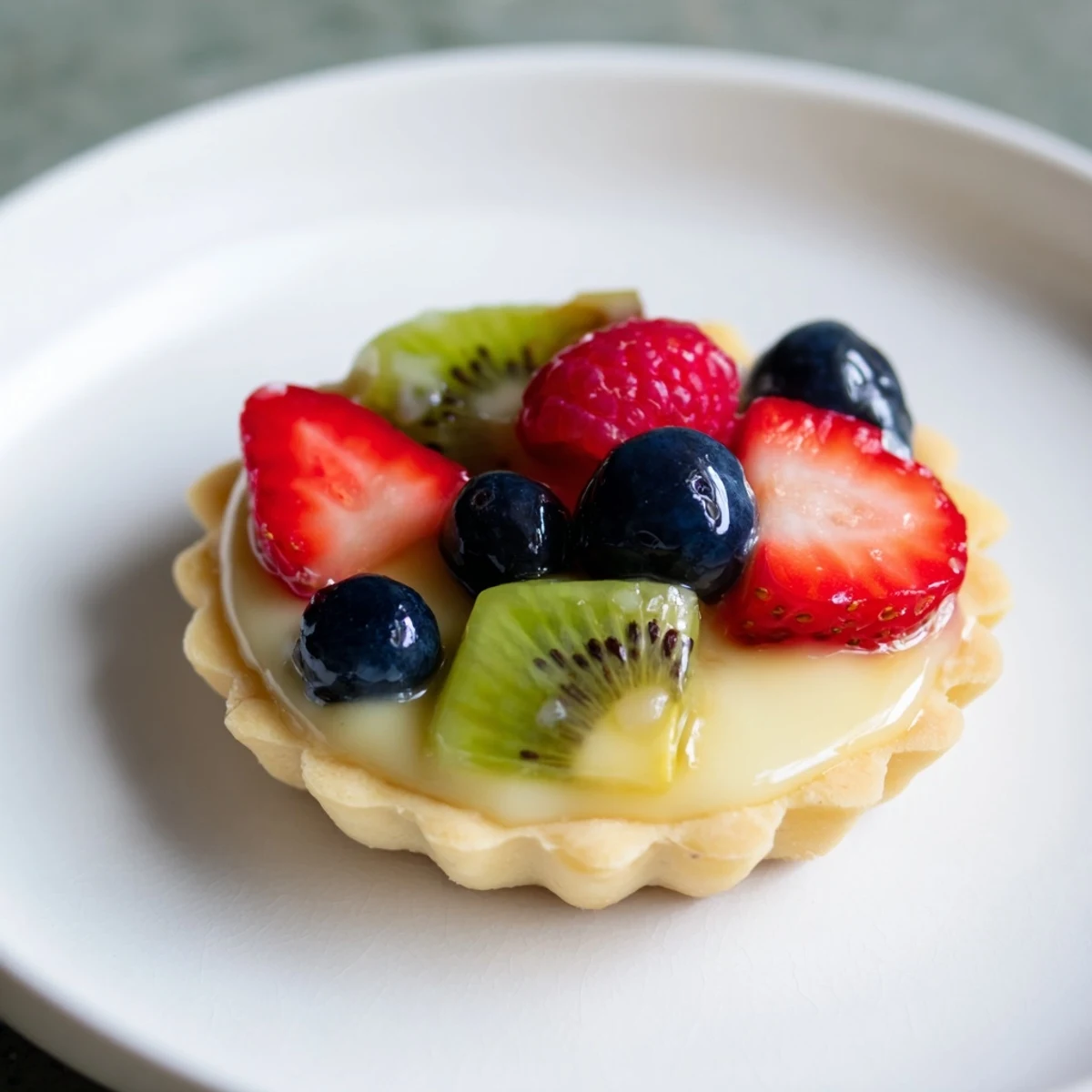 Mini fruit tartlets arranged in a circle, showcasing the vibrant colors of fresh summer berries on luscious pastry cream.