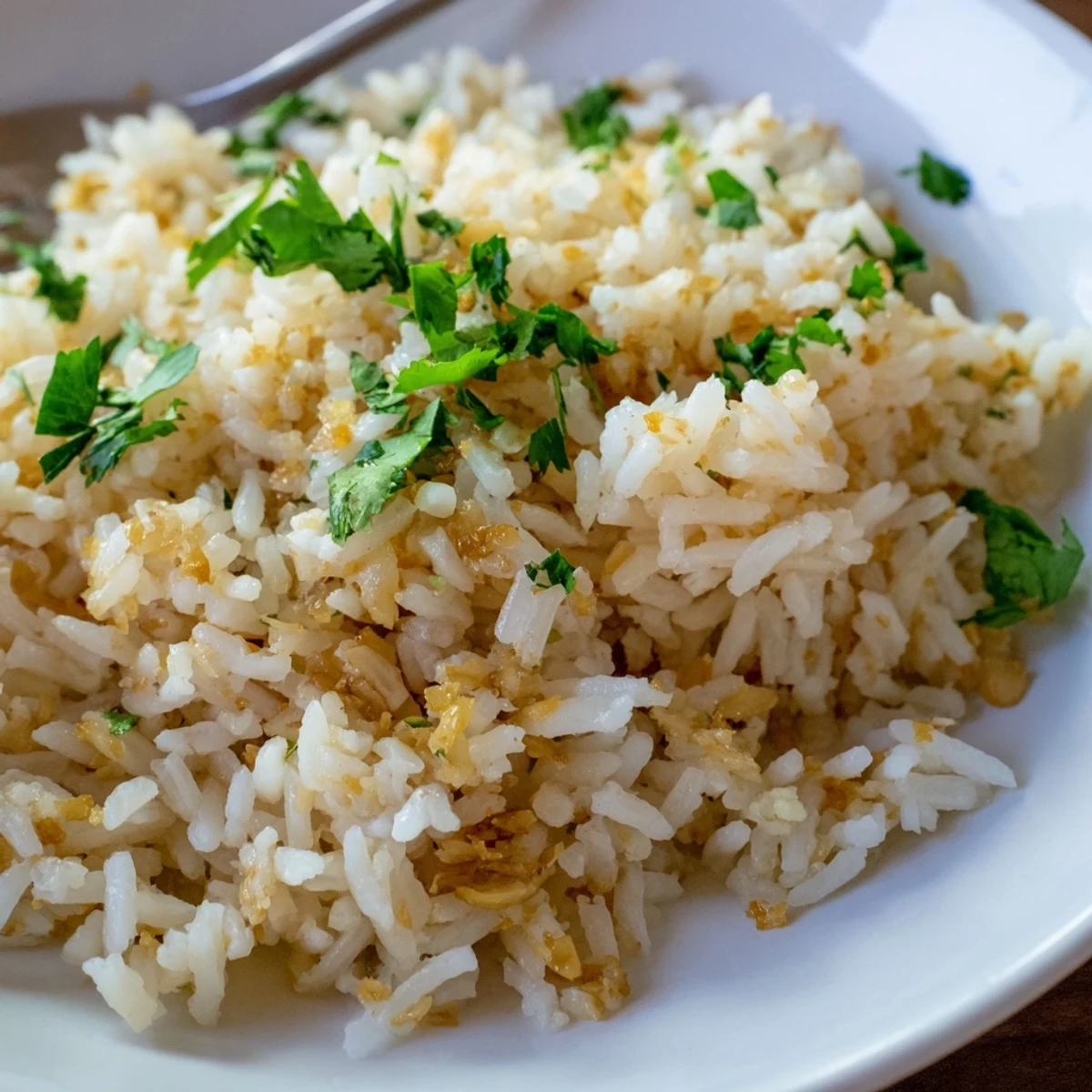 Fluffy jasmine rice with garlic oil is steamed in a saucepan for an aromatic, vegan side dish garnished with fresh cilantro.