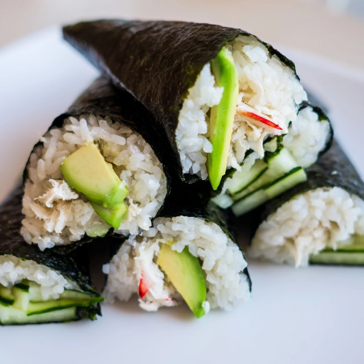 Homemade Sushi Rice Hand Rolls with avocado, cucumber, and crab, displayed on a wooden board with pickled ginger.