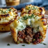 Individual mini shepherd's pies baked in muffin tins, topped with creamy mashed potatoes and savory ground beef filling.