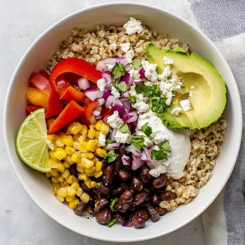 Colorful brown rice burrito bowl topped with black beans, bell peppers, corn, avocado, and queso fresco.  