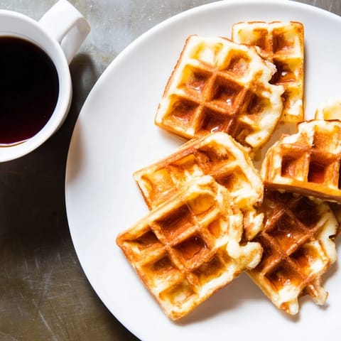 Crispy waffle quarters sit beside a bowl of rich syrup, a delicious American brunch.