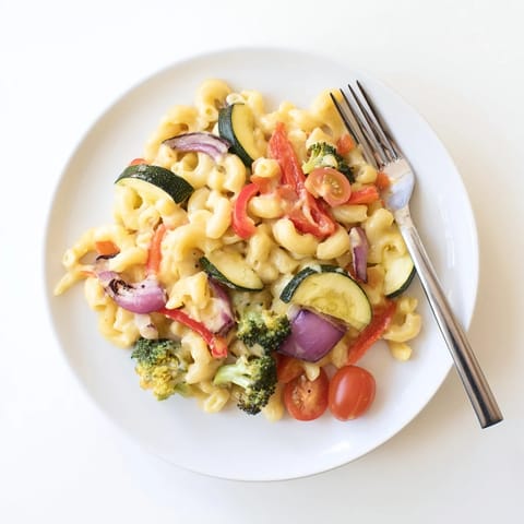 A hearty bowl of roasted veggie mac & cheese is garnished with extra Parmesan, showcasing tender elbow macaroni coated in a velvety sharp cheddar and mozzarella sauce.