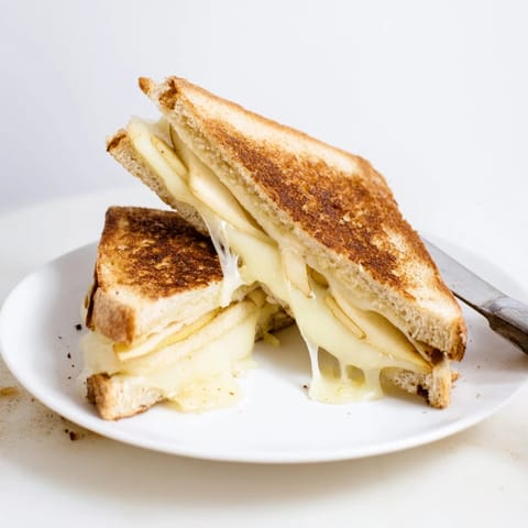 A close-up of a toasted sandwich with smoky Gouda, crisp apple slices, and melty cheese oozing between buttery bread.  