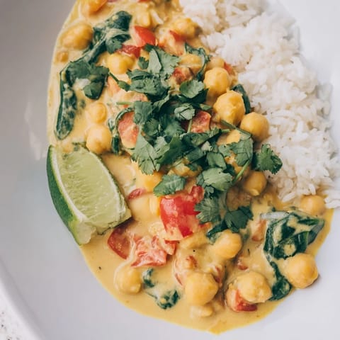 A steaming bowl of creamy chickpea curry, garnished with fresh cilantro and lime wedges, served alongside fluffy basmati rice.  