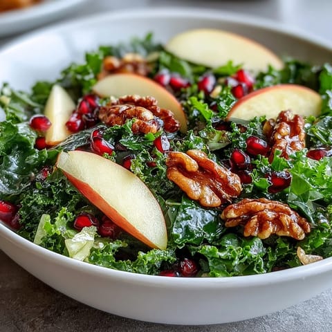 Freshly massaged kale topped with crisp apple slices, ruby-red pomegranate seeds, and chopped walnuts tossed in a tangy apple cider vinaigrette.