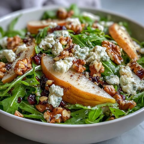Arugula and Pear Bowl served as a light lunch, with crumbled goat cheese, chopped pecans, and a honey-Dijon vinaigrette on a white ceramic plate.