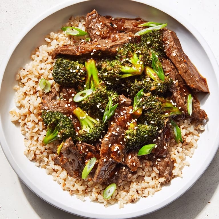 Steaming bowl of slow-cooker beef & broccoli with fluffy brown rice and fresh greens, ready to eat.