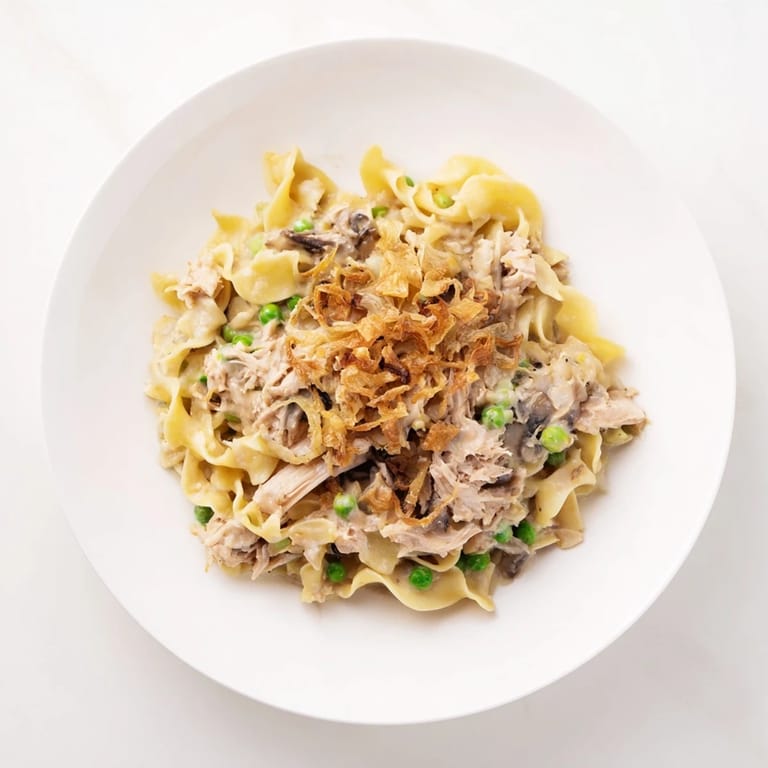 A close-up view of creamy tuna noodle casserole topped with crispy onions, bubbling inside a baking dish.
