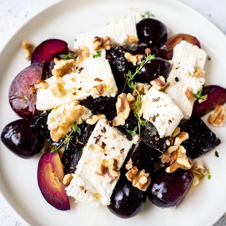 A beautiful Midnight Orchard arrangement, featuring vibrant plums, grapes, and ash-covered goat cheese for serving.