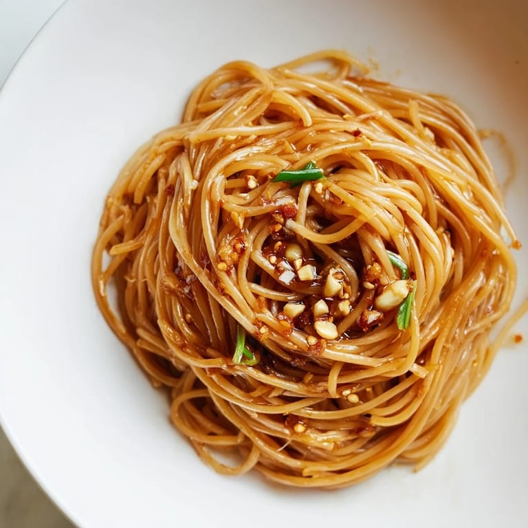 Close-up of freshly tossed Garlic Chili Oil Noodles, with visible chili flakes and sesame seeds, a flavorful meal.
