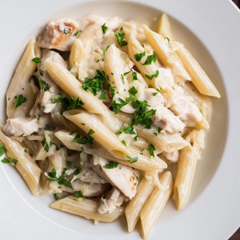 Serving suggestion for Roasted Garlic Chicken Penne, garnished with fresh parsley and grated Parmesan alongside a glass of white wine.