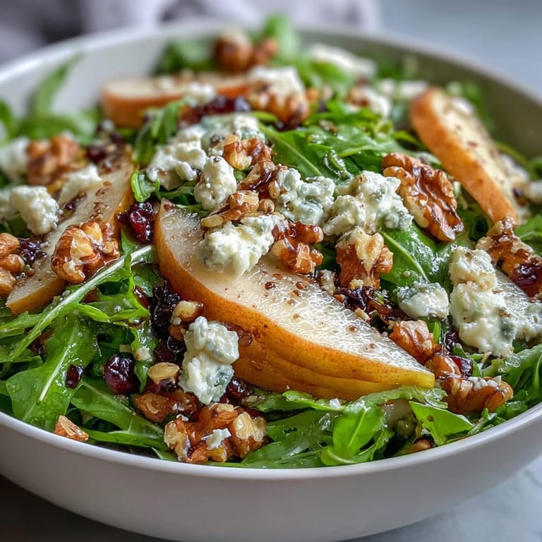 Arugula and Pear Bowl served as a light lunch, with crumbled goat cheese, chopped pecans, and a honey-Dijon vinaigrette on a white ceramic plate.