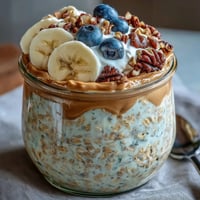 Creamy High-Protein Peanut Butter Overnight Oats in a glass jar topped with banana slices and chopped peanuts.
